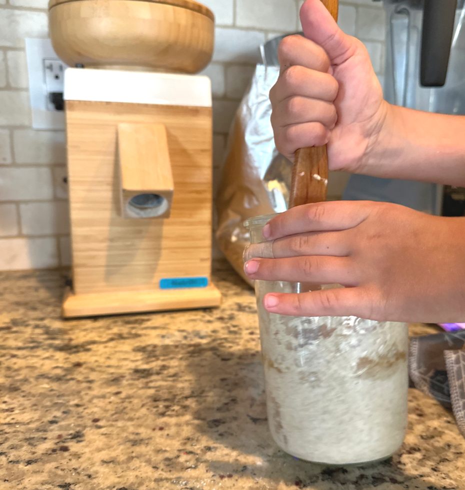 girl stirring sourdough starter with grain mill in background tough kid