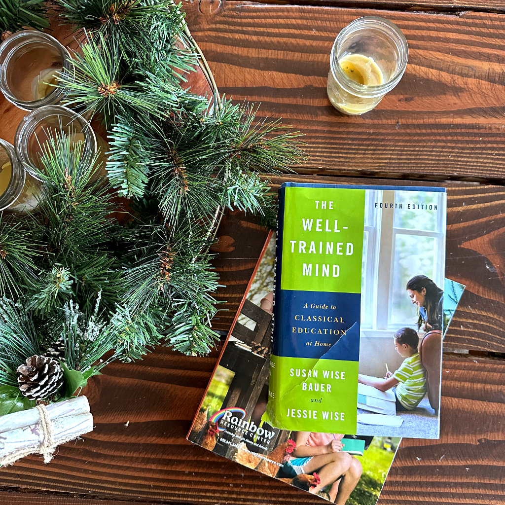 green wreath with candles on dining room table with books. The well trained mind and Rainbow Resource catalog. Homeschooling resources for homeschooling multiple kids. 